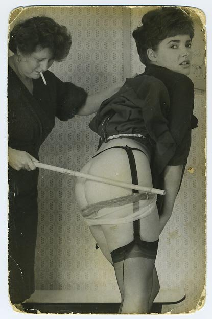 young woman in nice lingerie gets a bamboo caning from a weary older woman with a cigarette hanging out of her mouth